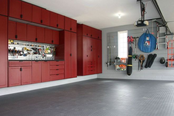 Modern garage with red cabinets, gray floor, and wall-mounted tools and sports gear