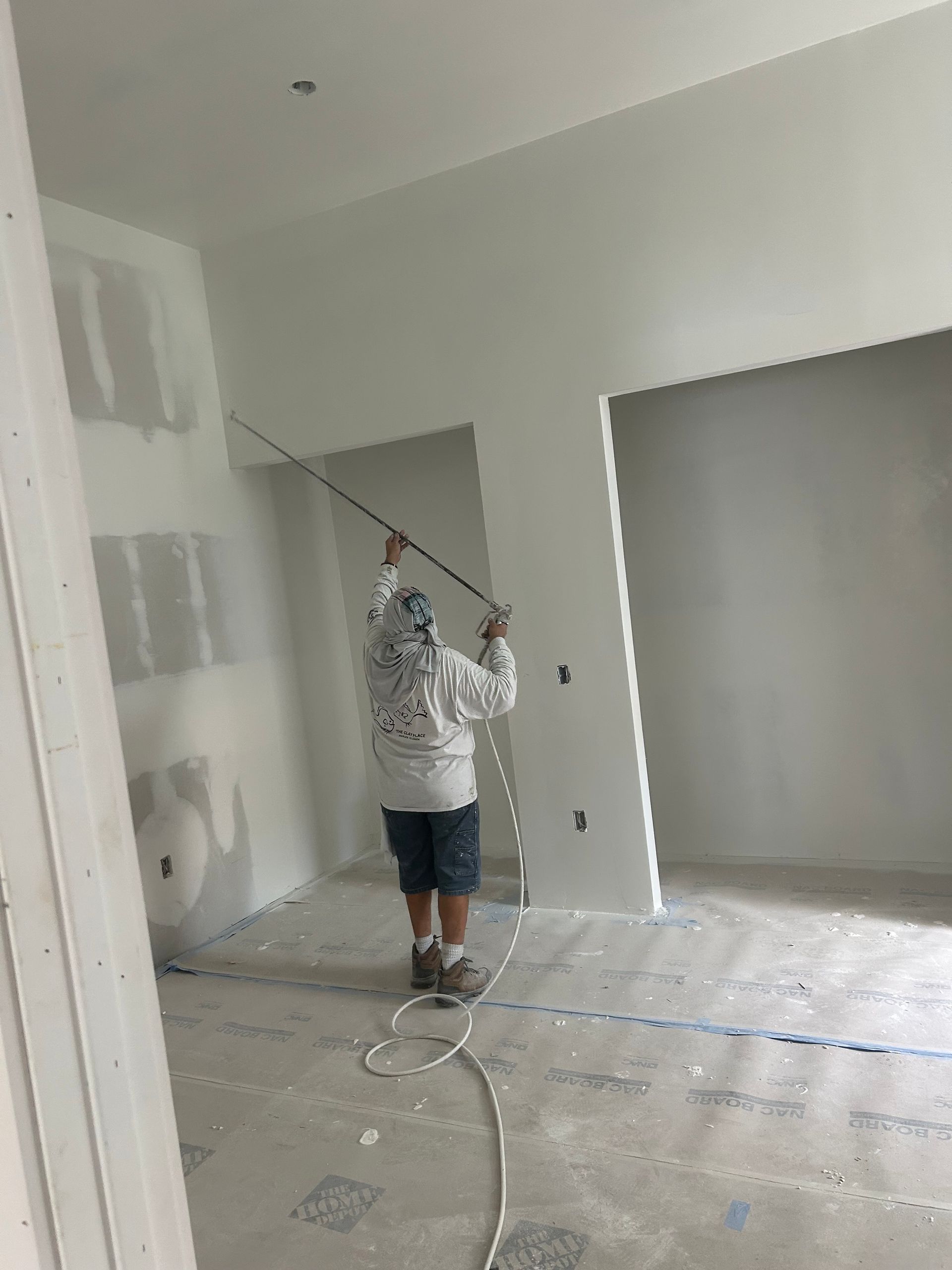 Person painting a light-gray room with a roller, standing on a floor covered with drop cloths.