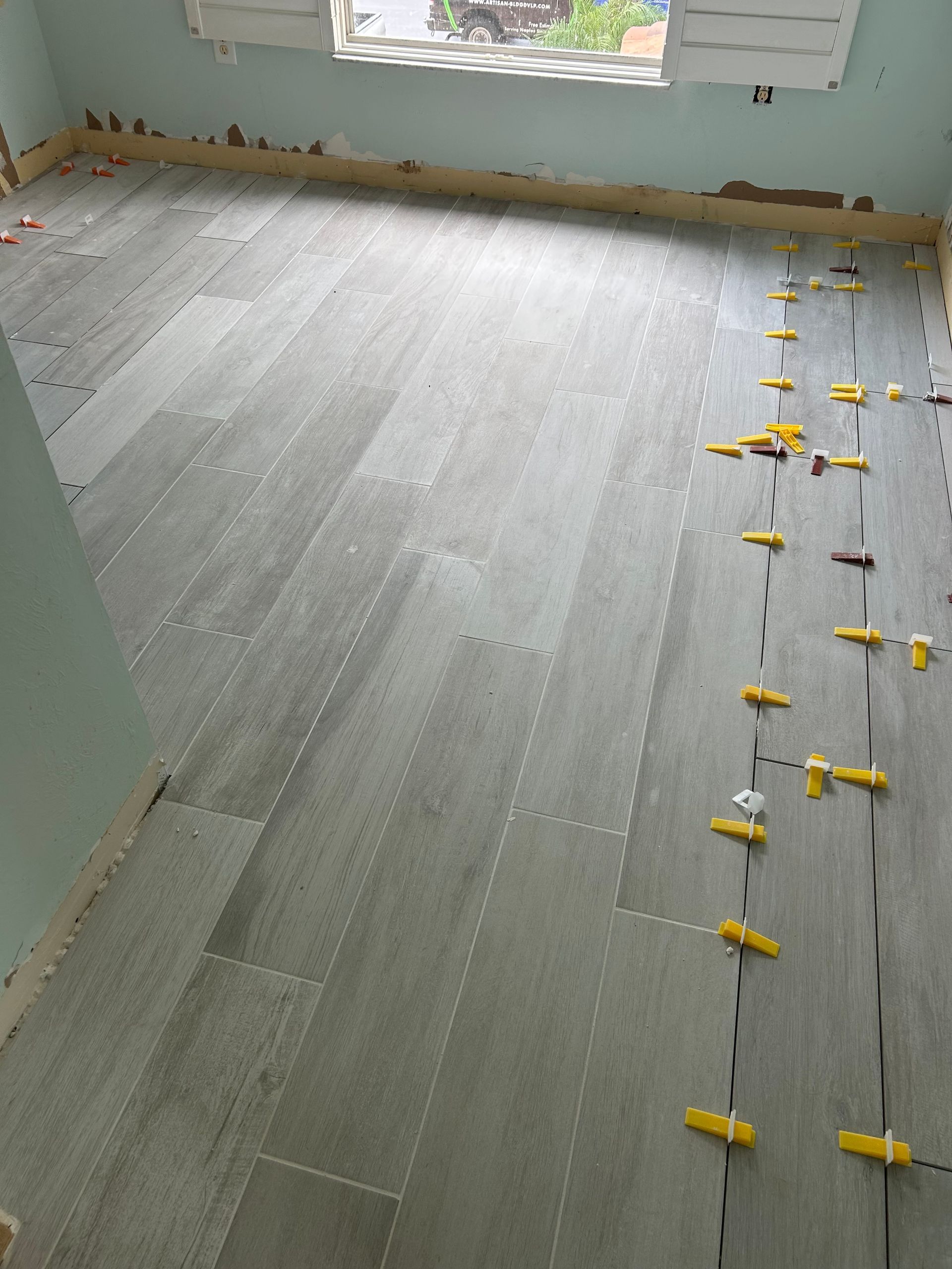 Floor tile installation in progress in an empty room, with yellow spacers along the seams.