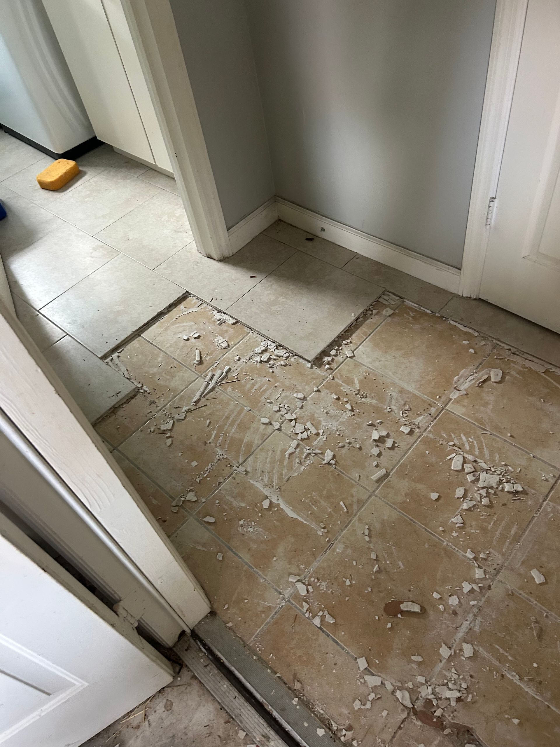 Damaged hallway floor with missing tiles and debris near a doorway
