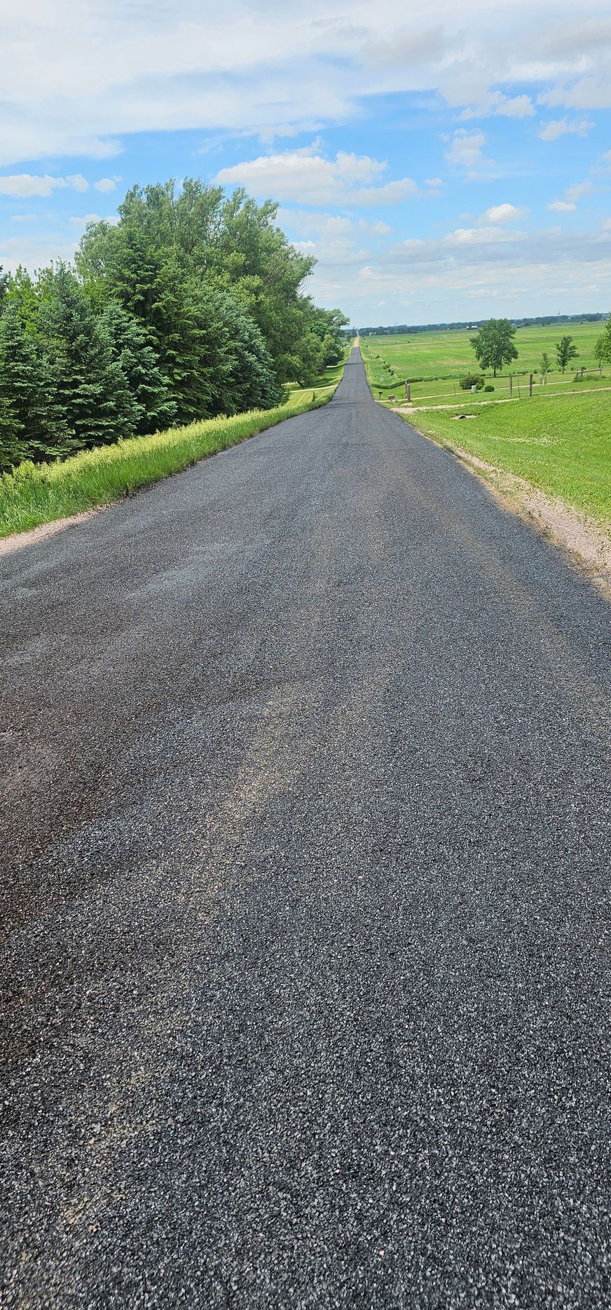 Gravel road stretching into the distance through green fields under a partly cloudy sky