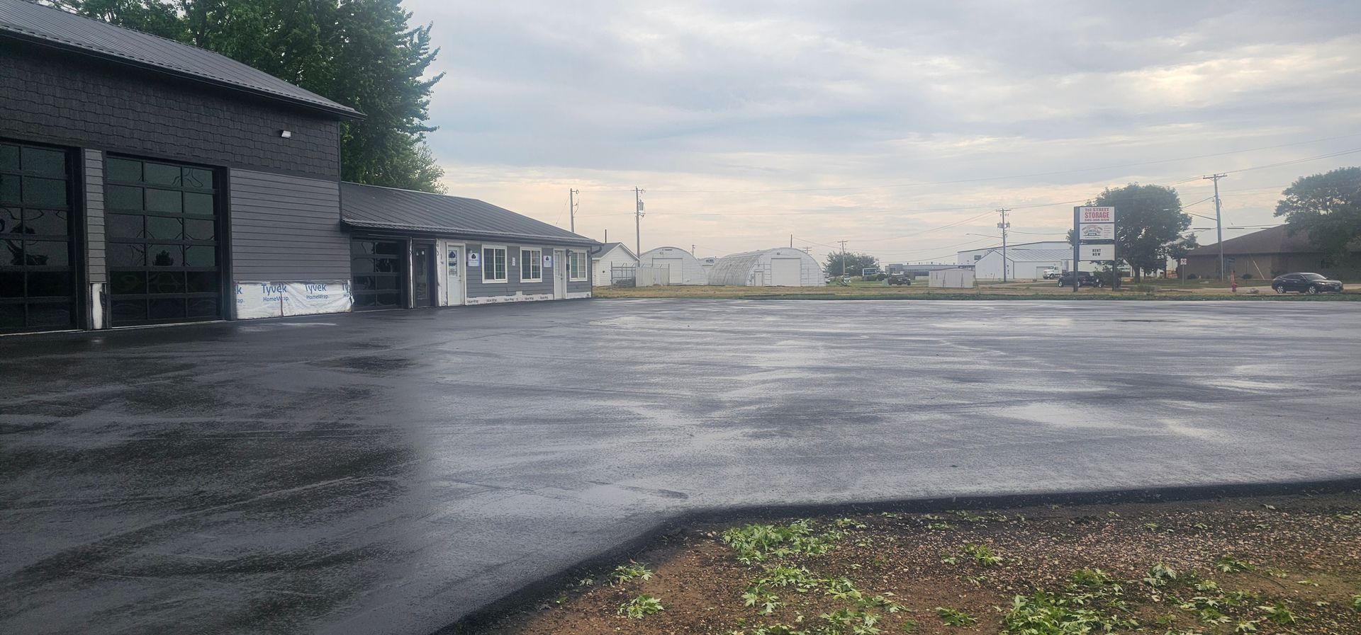 Empty wet parking lot beside low buildings under a cloudy sky.