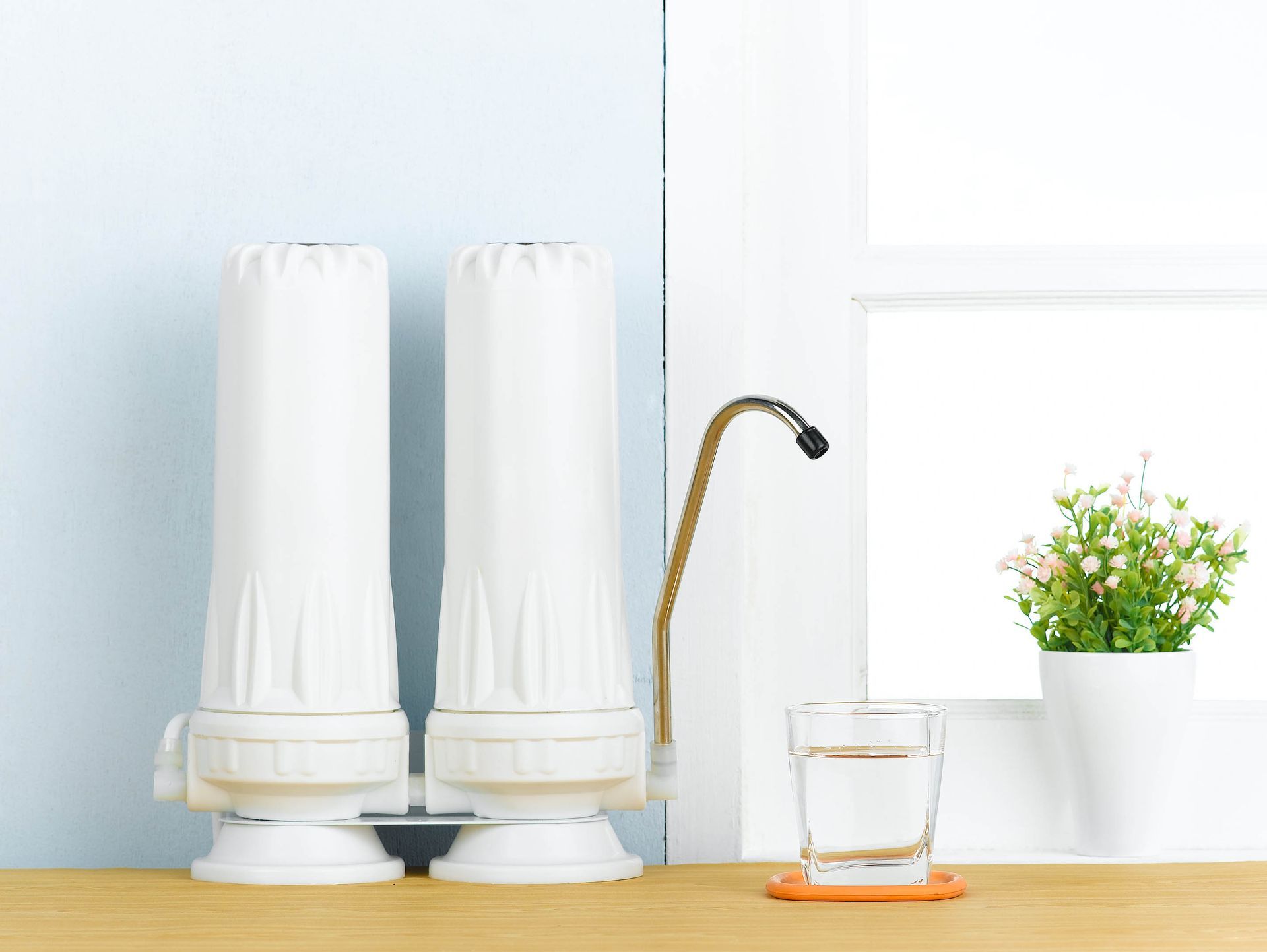 Two white kitchen canisters beside a faucet, with a glass on an orange coaster and a small potted plant