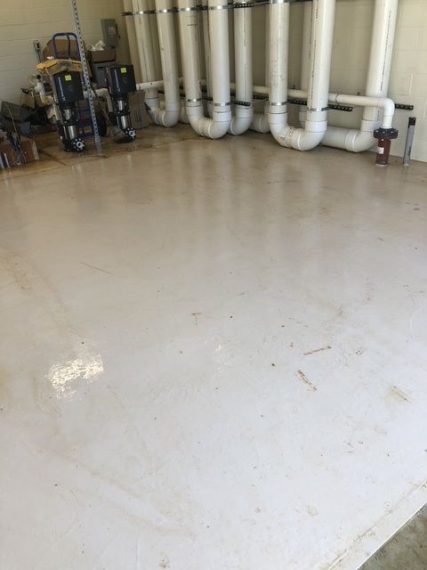 Basement utility room with white floor, pipes along the wall, and cleaning equipment.