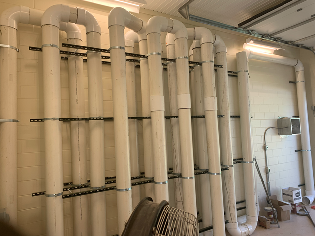 White industrial ventilation ducts and hoses stacked along a warehouse wall, with tools and equipment nearby.