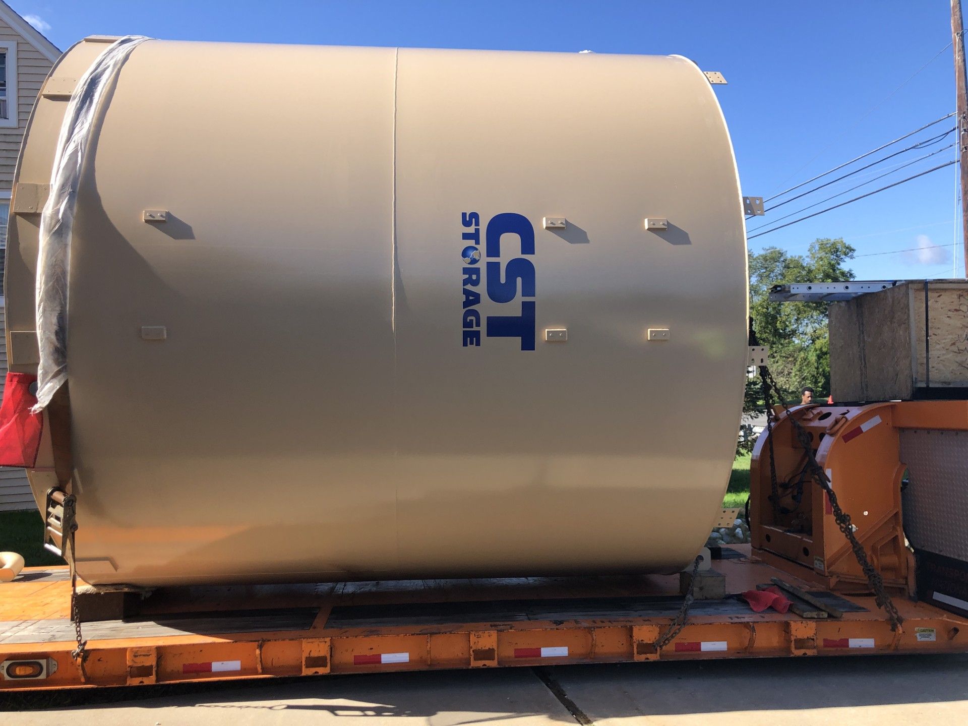 Large beige industrial tank labeled “CST Storage” on a trailer outdoors under a blue sky