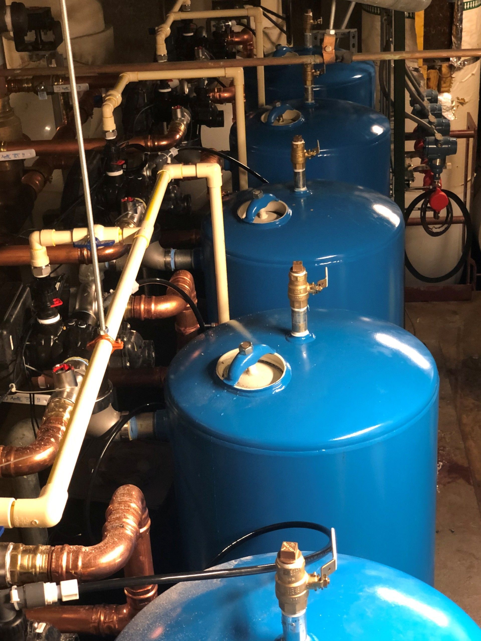 Row of blue industrial tanks and copper pipes in a utility room