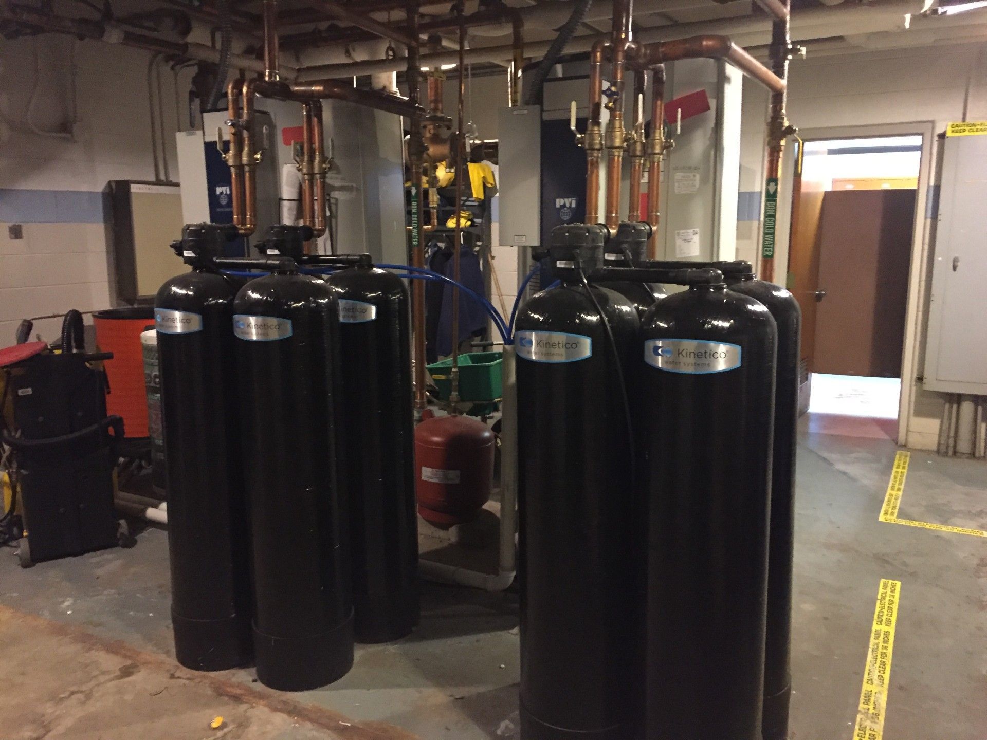 Industrial room with three large black cylindrical tanks and exposed pipes in the background