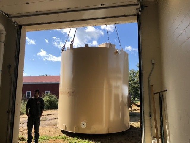 Large beige cylindrical tank suspended in a garage doorway, with a person standing to the left.