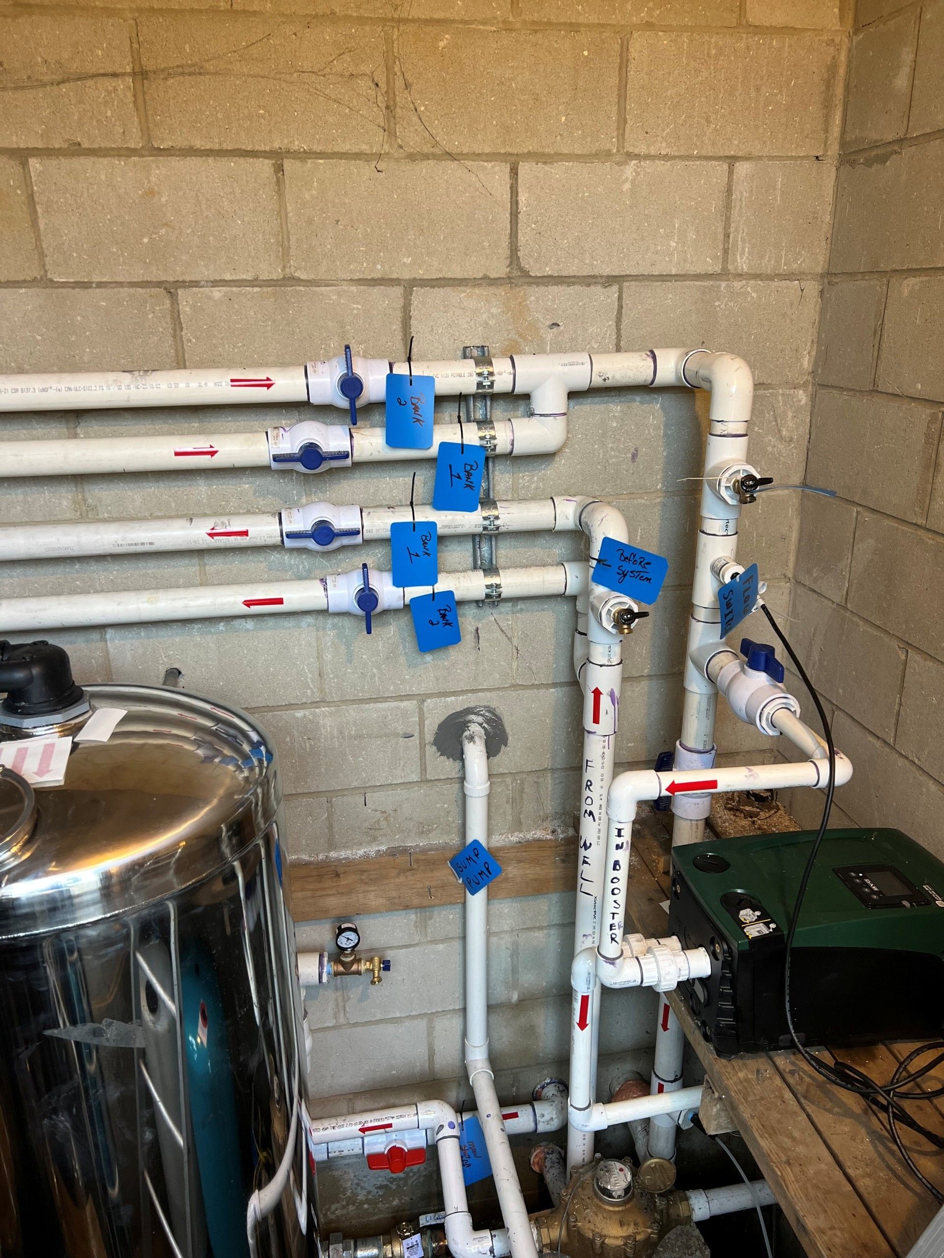 Plumbing pipes with blue valves mounted on a cinderblock wall in a utility room.