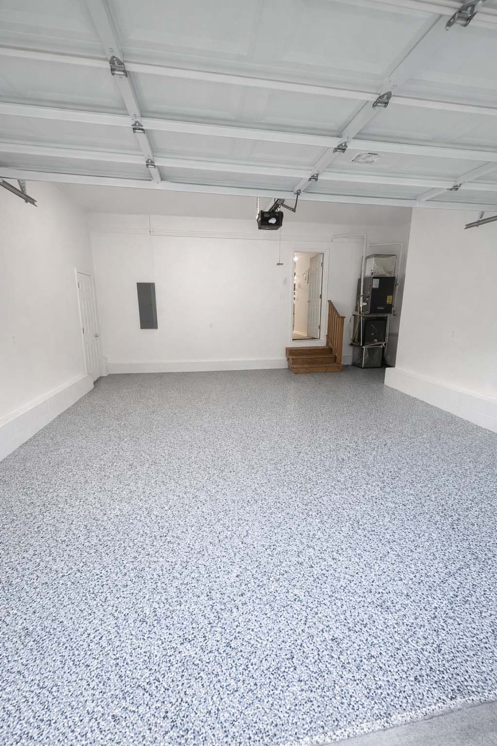 Empty garage with white walls, exposed ceiling, and speckled epoxy floor, viewed toward a doorway.
