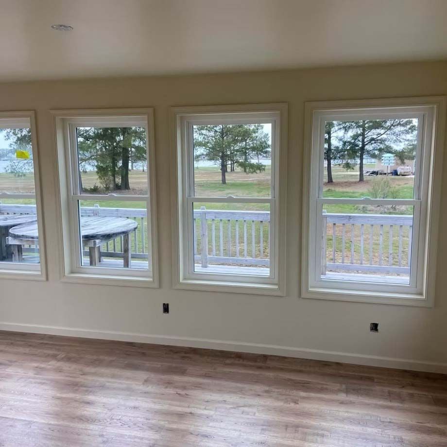 Empty room with wood floors and four windows overlooking a porch and yard