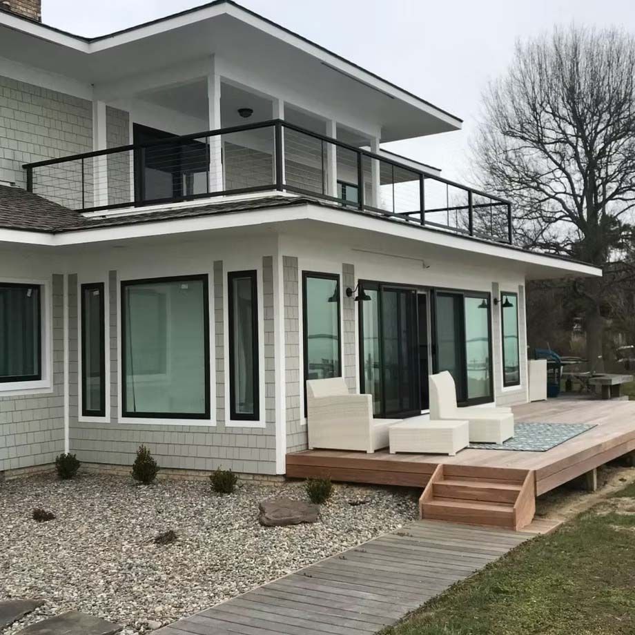 Modern two-story house with white siding, black railings, and a small deck on a gravel yard