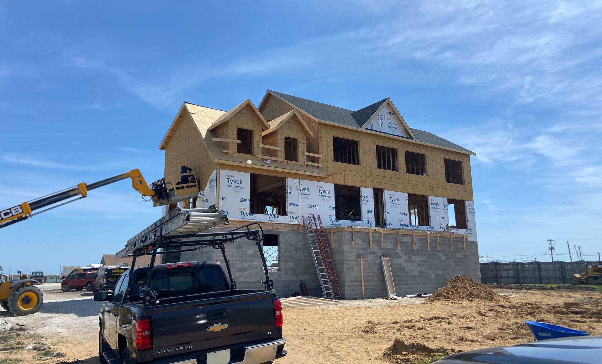 Partially built house under construction with workers' vehicles and a crane on a dirt lot