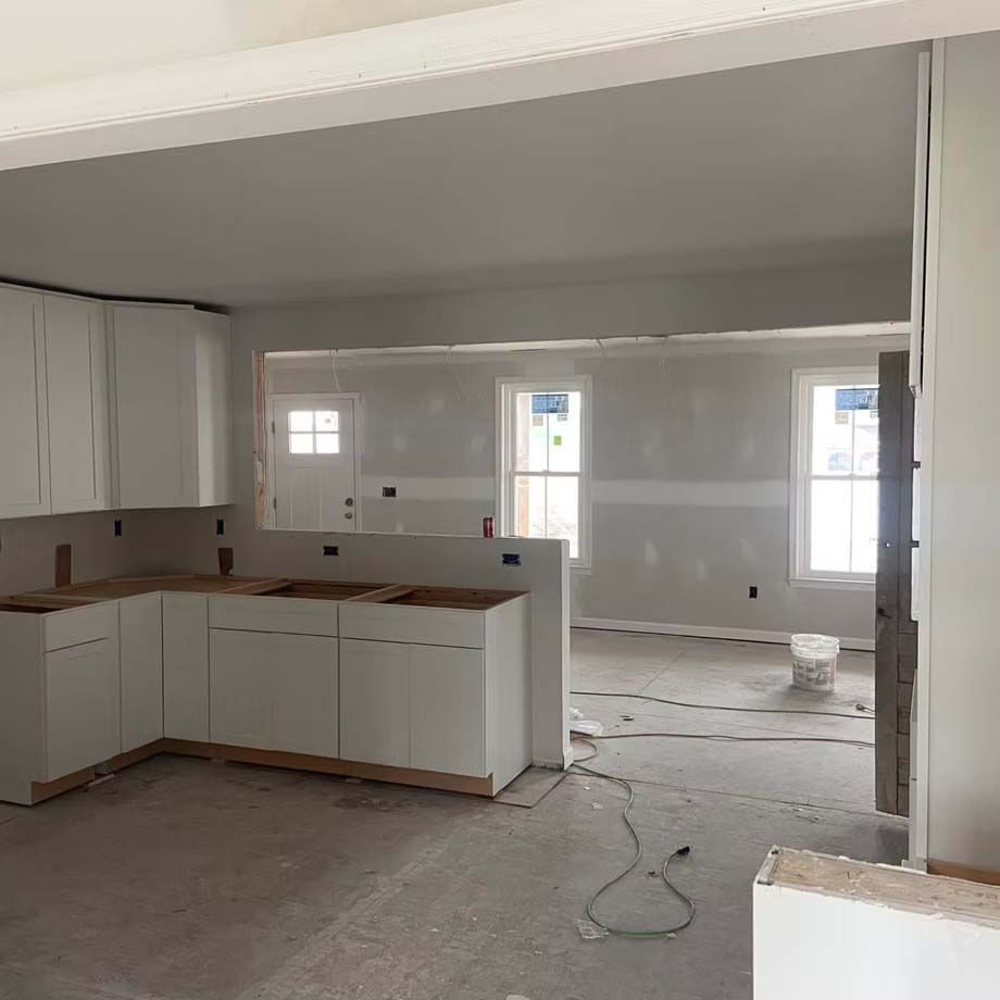 Unfinished kitchen and living area with white cabinets, bare floors, and exposed walls during renovation
