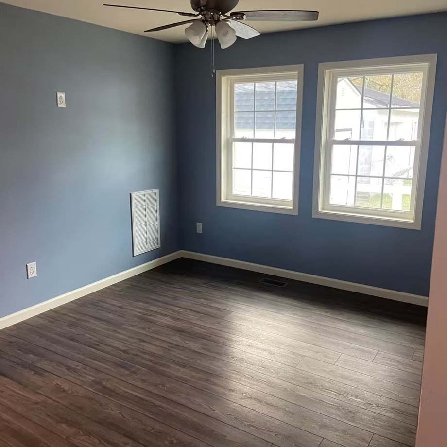 Empty blue bedroom with dark wood floors, two windows, and a ceiling fan
