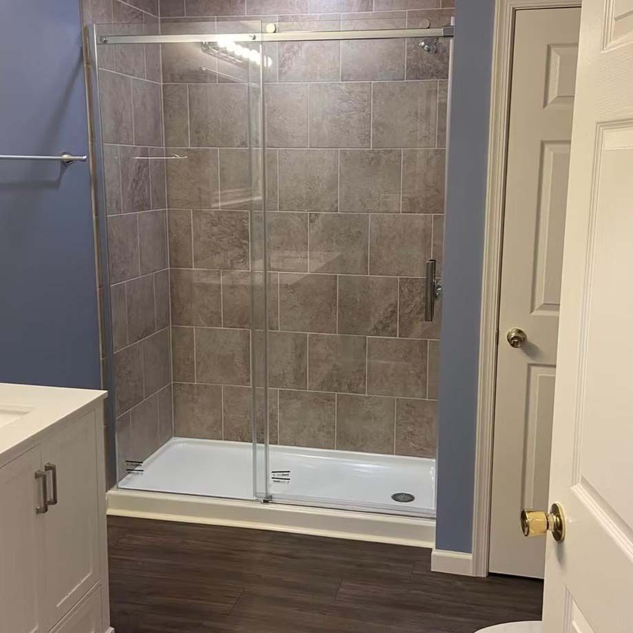 Glass walk-in shower with beige tile walls, white base, and dark wood-look bathroom floor