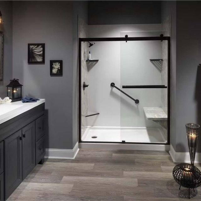 Modern gray bathroom with a glass walk-in shower and dark vanity, lit by lanterns and wall decor.