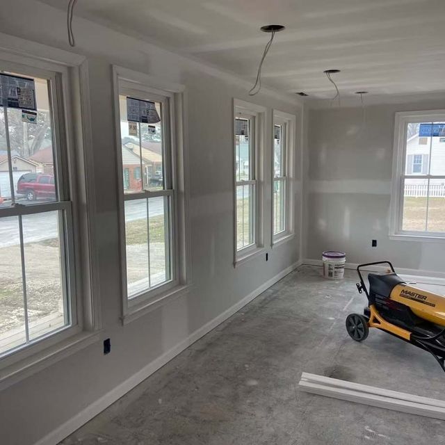 New home interior with unfinished gray floor, white walls, windows, and a yellow floor machine.