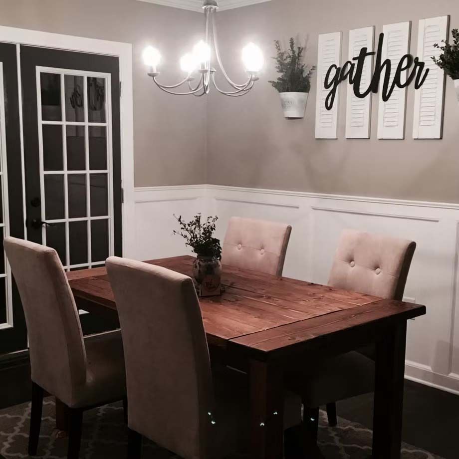 Dining room with wooden table, beige chairs, chandelier, and wall decor reading “gather”