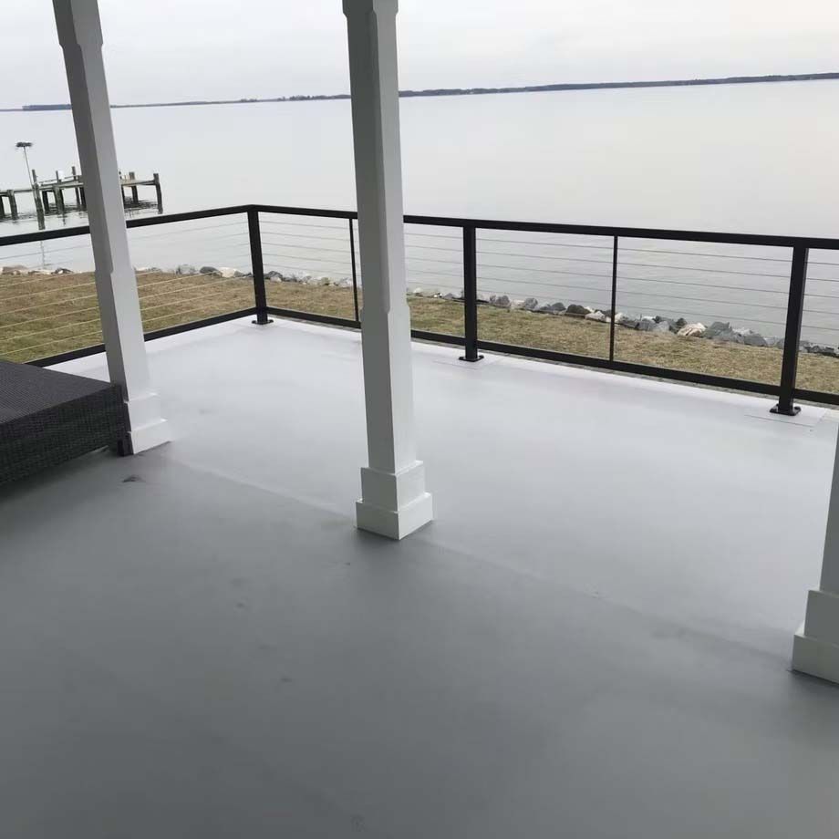 Covered waterfront deck with gray floor, black railing, and white columns overlooking calm water