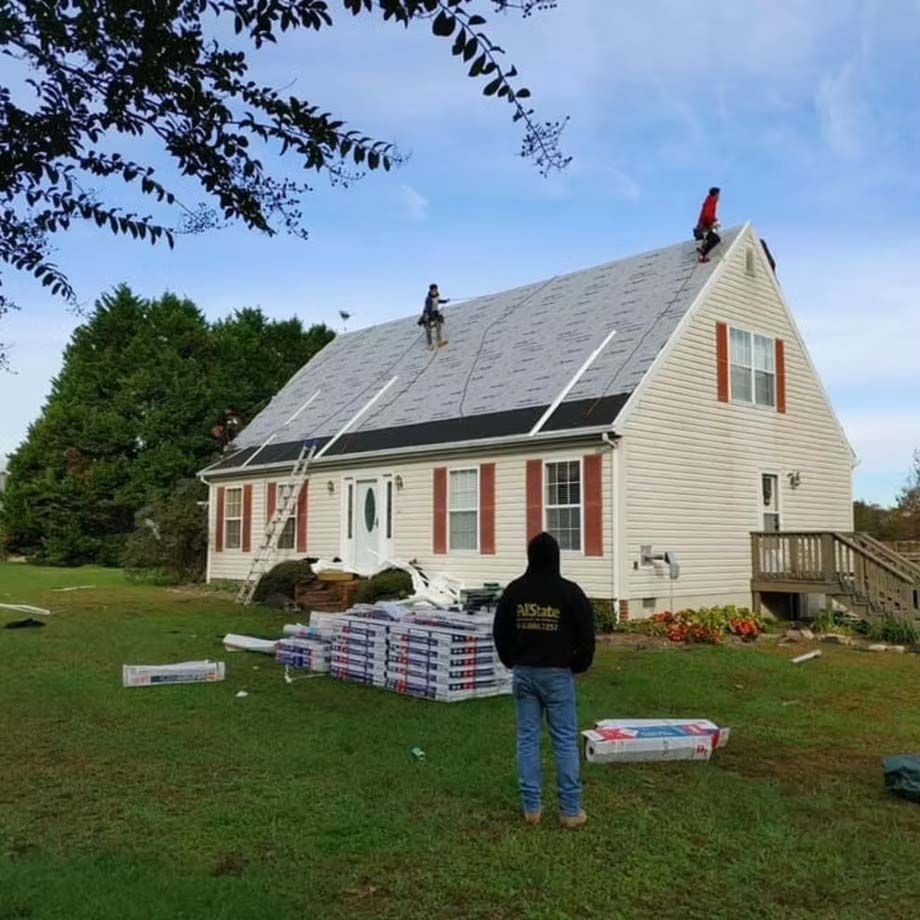 Two people on a lawn installing solar panels on a white house with red shutters and boxes of supplies.