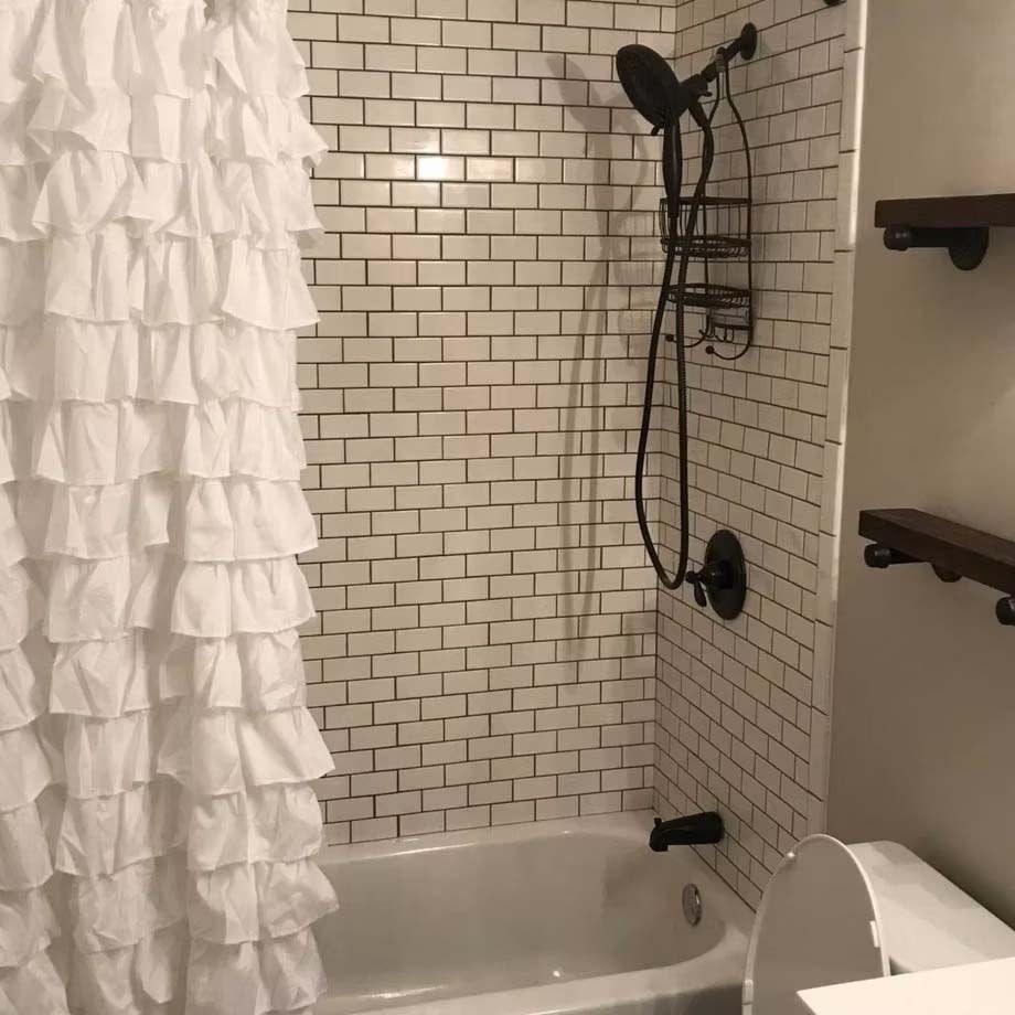 Small bathroom with white tile shower, ruffled curtain, and toilet beside a bathtub.