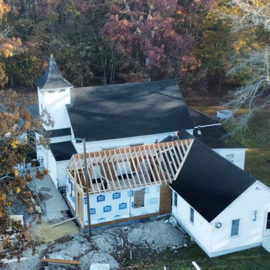 Aerial view of a house under roof repair with exposed rafters and autumn trees nearby