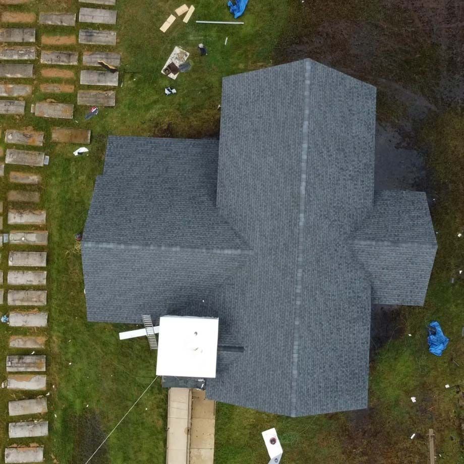 Aerial view of a gray-roofed house with a driveway, yard, and scattered objects around it.