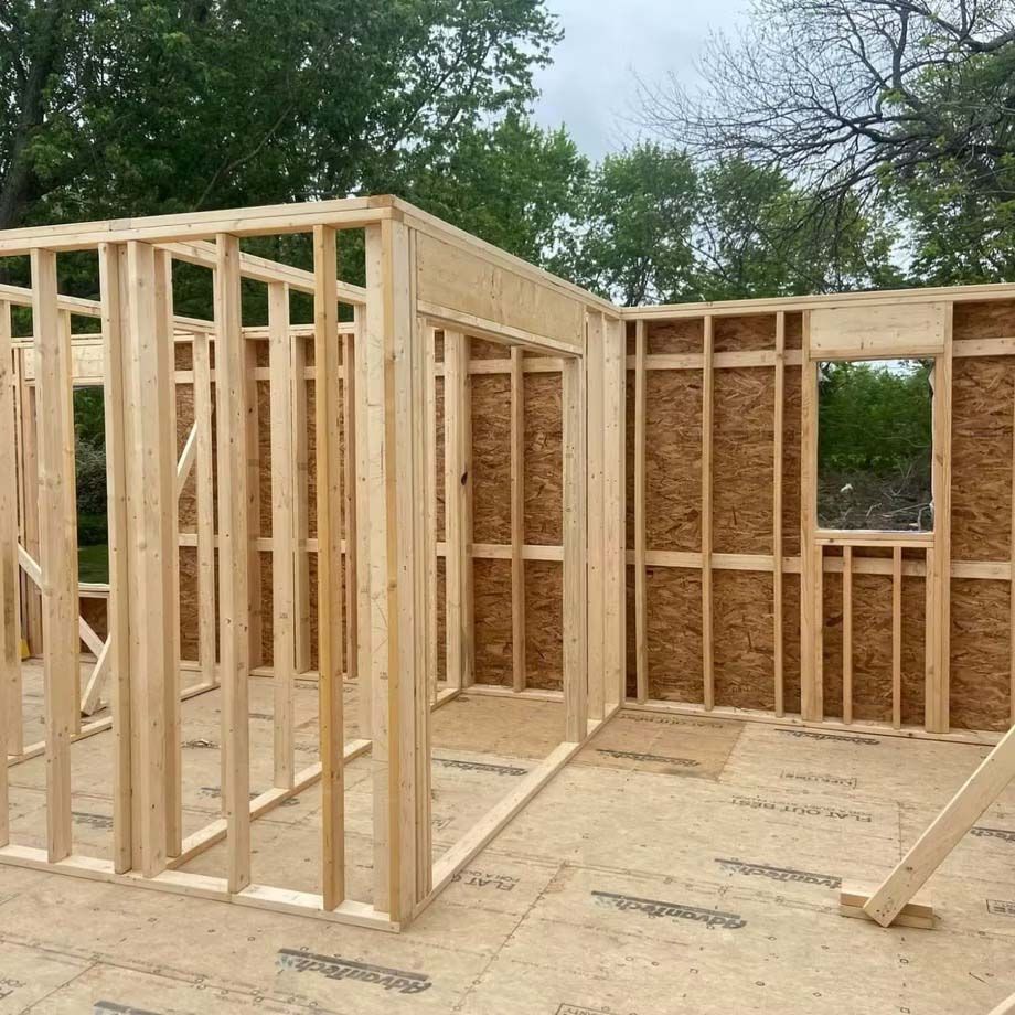 Wood-framed house under construction with unfinished walls and floor in a wooded area