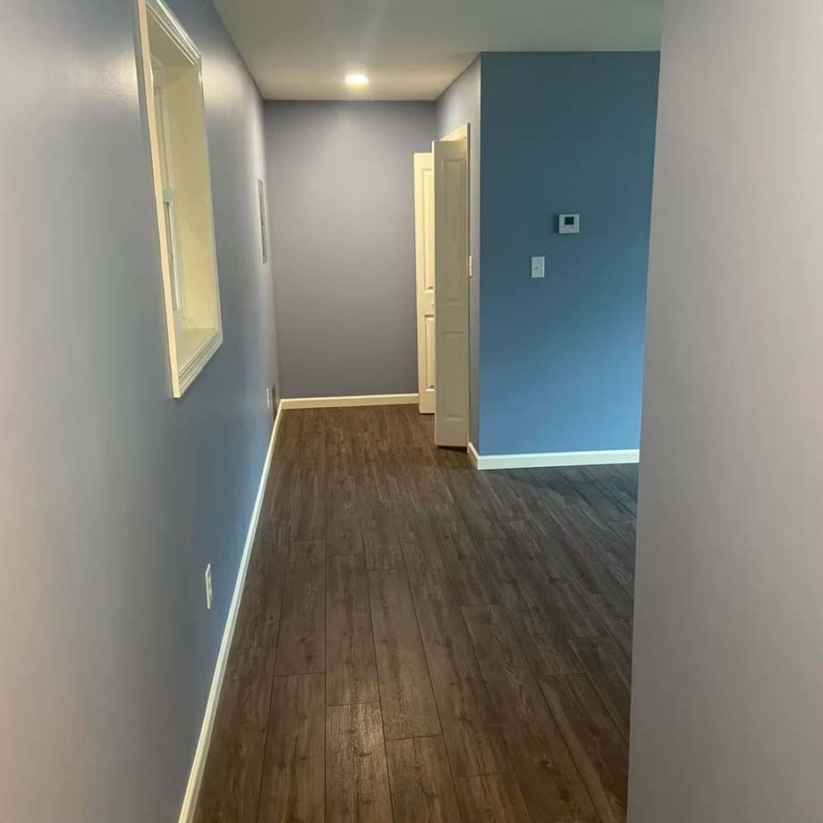 Empty hallway with blue walls, dark wood flooring, and a doorway at the end.