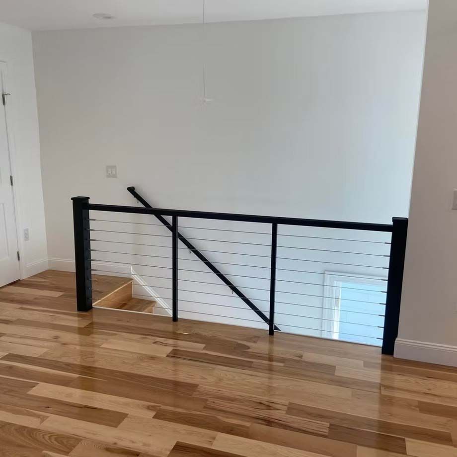 Interior hallway with a black metal railing and wood flooring, overlooking stairs below