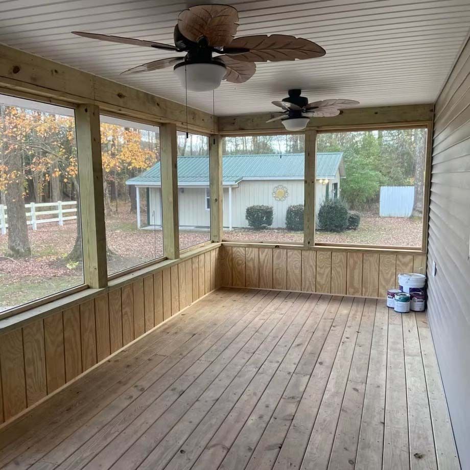 Screened wooden porch with two ceiling fans, open windows, and cleaning supplies in the corner.