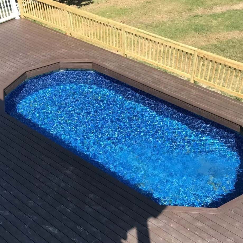 An above-ground pool with bright blue water set into a wooden deck, beside a grassy yard and fence.
