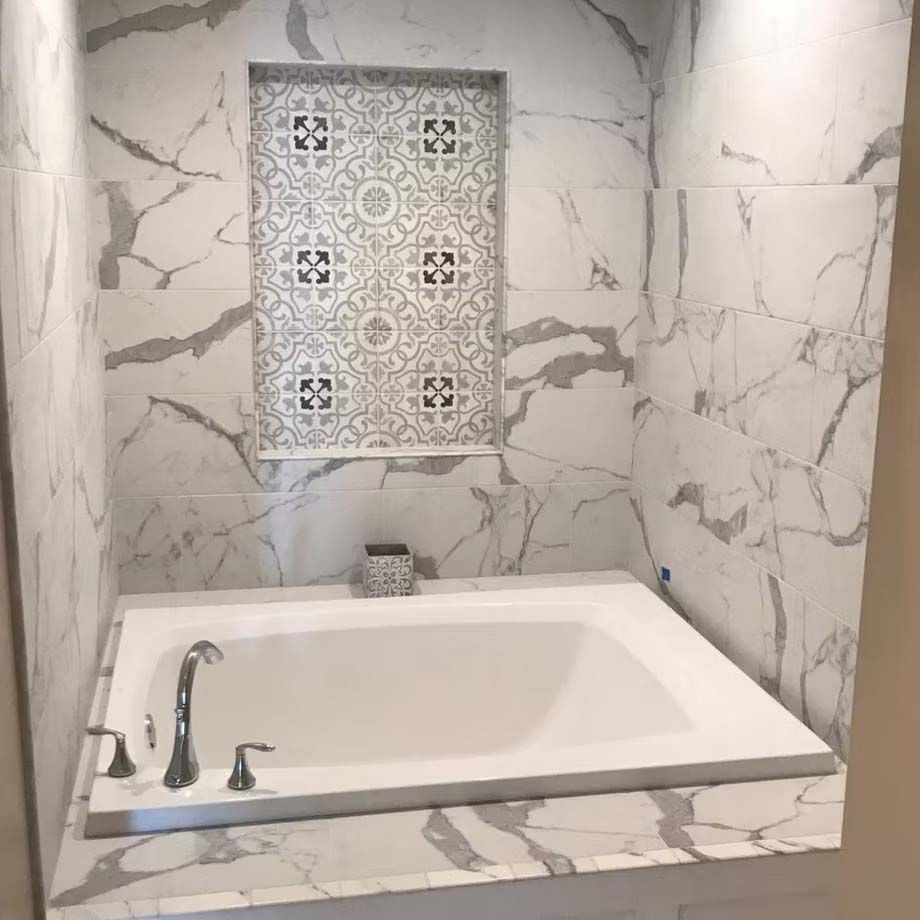 White marble bathroom with a soaking tub and decorative tile niche above it