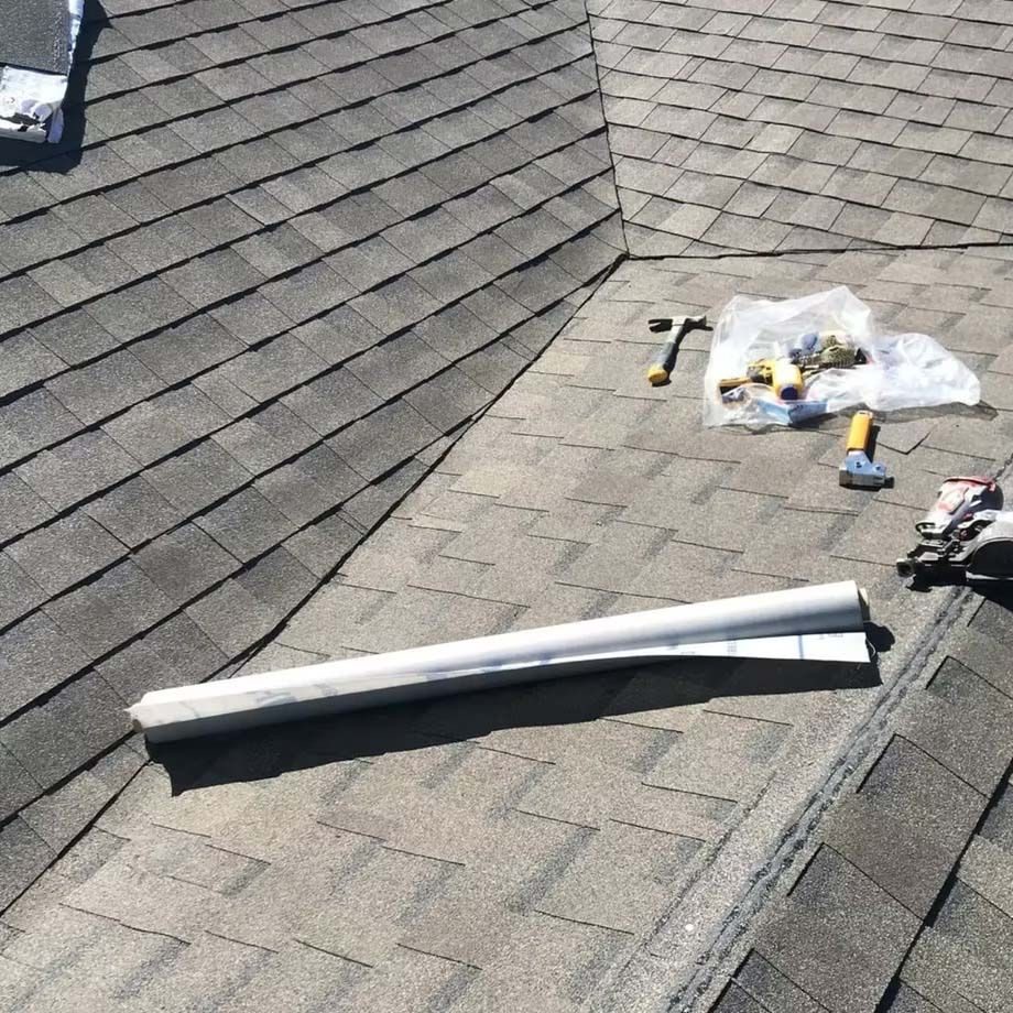 Roof shingles with tools, a white gutter section, and roofing supplies during repair work