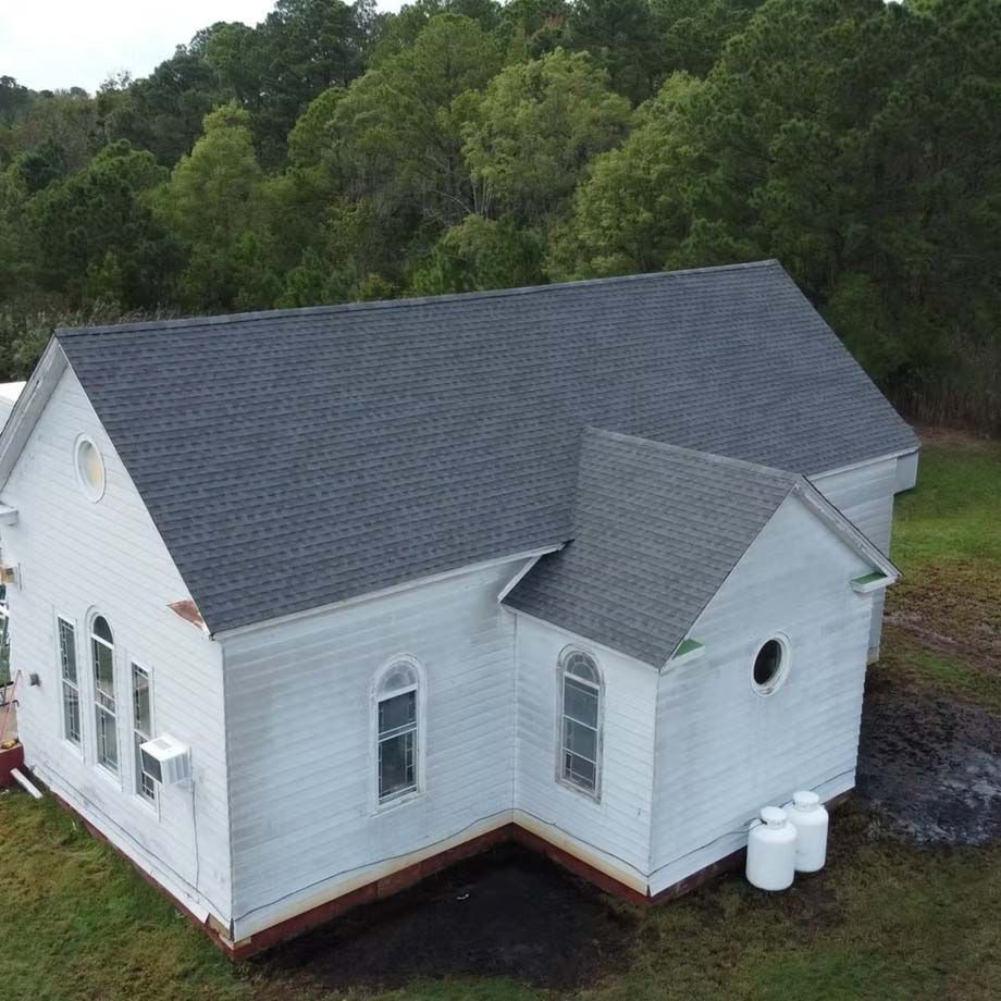 White house with dark gray roof beside a wooded hillside, seen from above