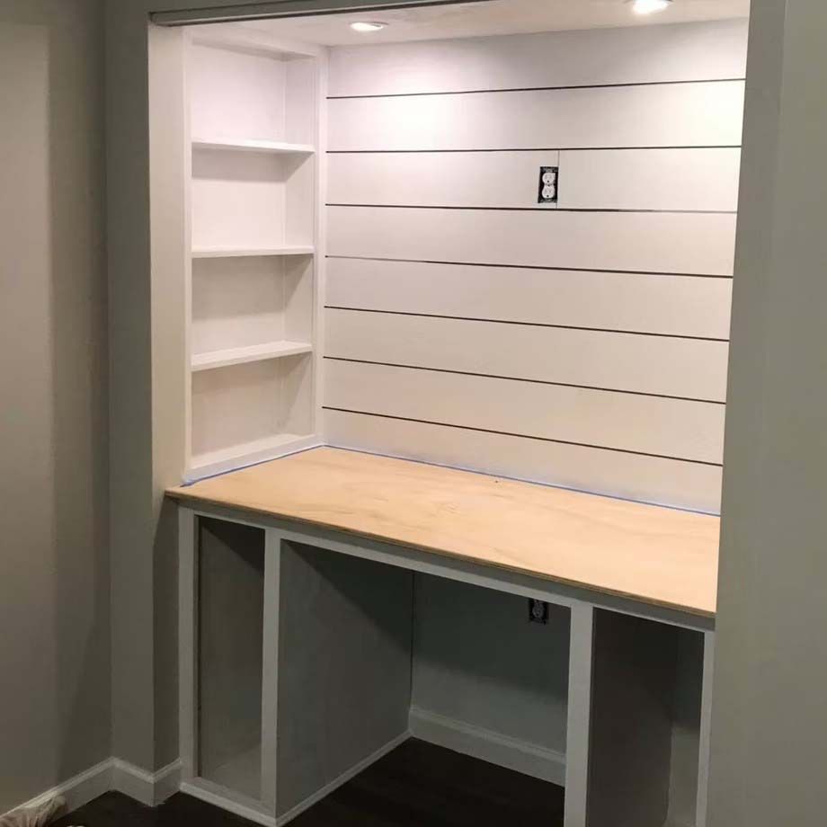 Built-in white desk nook with shelves and wood countertop in an empty room