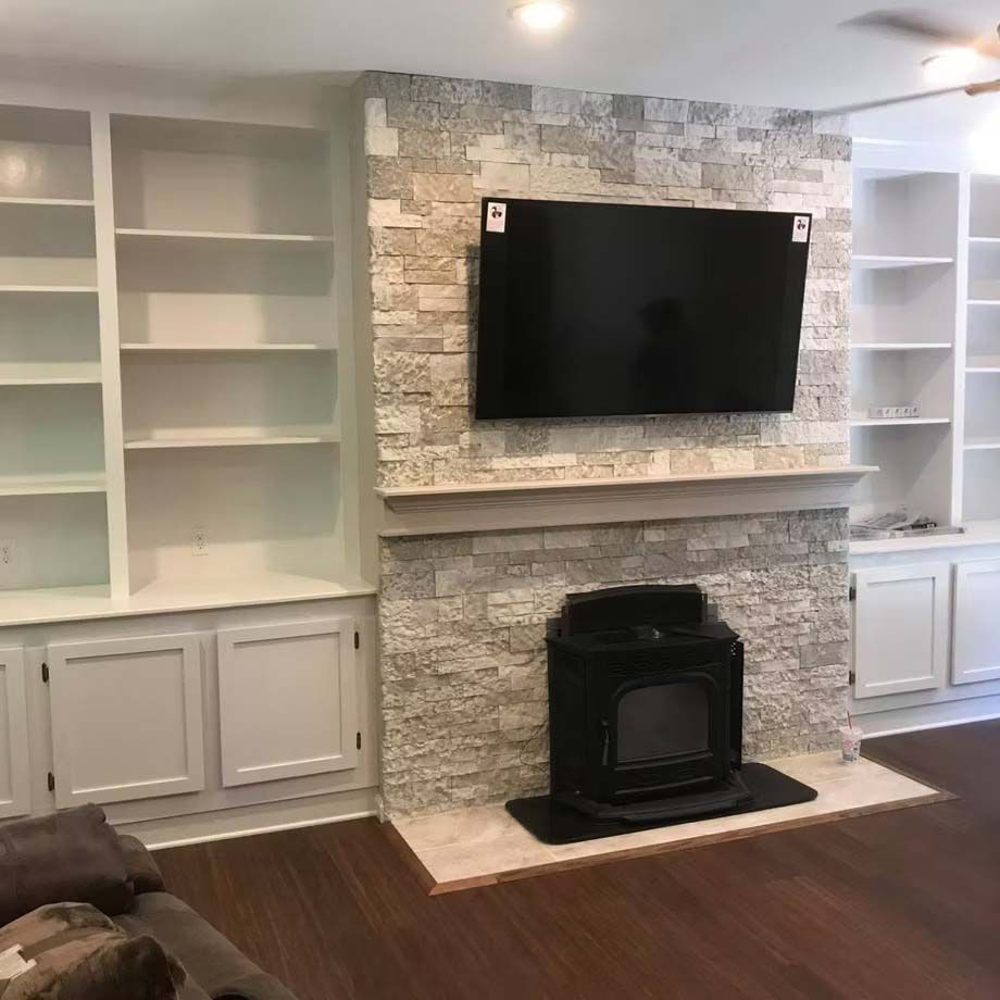 Living room with built-in shelves, stone fireplace, wall-mounted TV, and white cabinetry