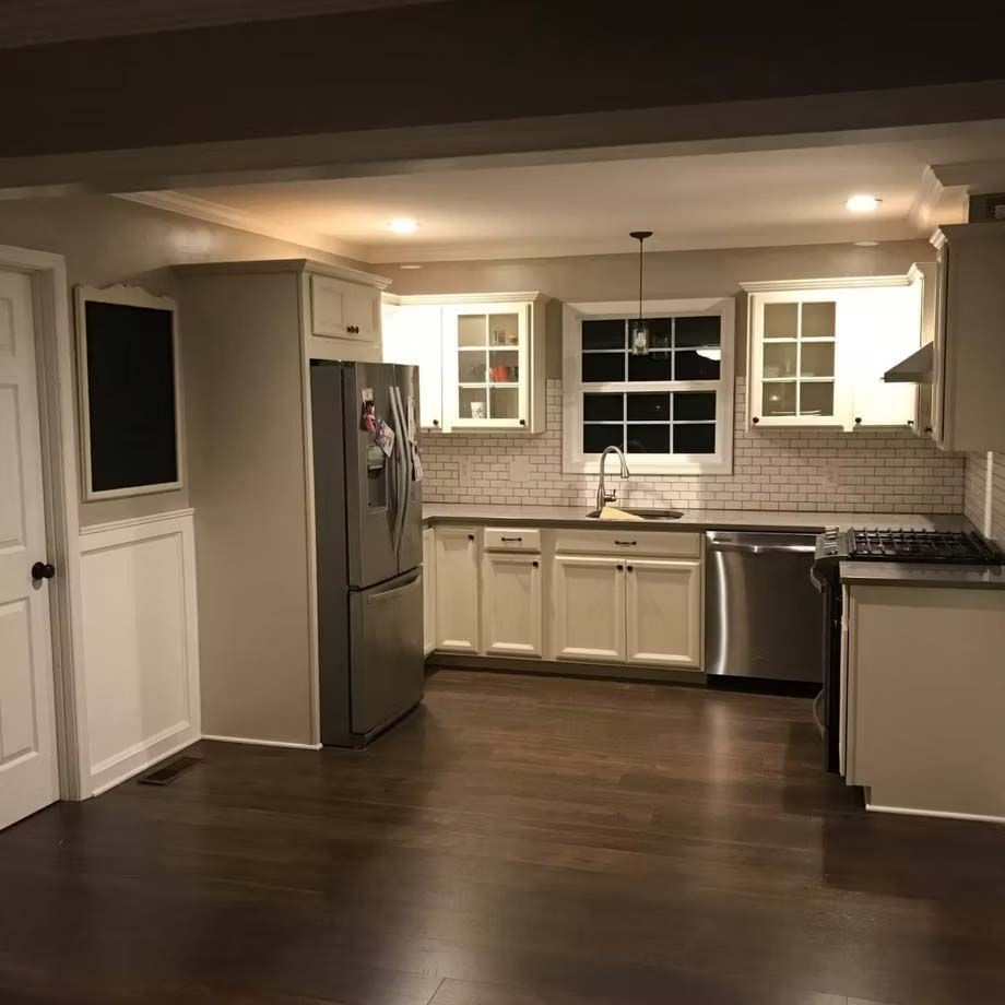 Empty modern kitchen with stainless steel fridge, white cabinets, and dark wood floors at night