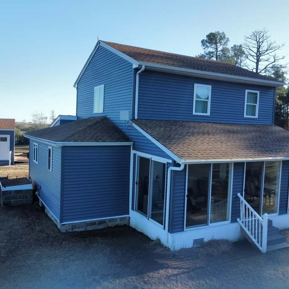 Blue two-story house with a screened porch and front steps in a gravel yard