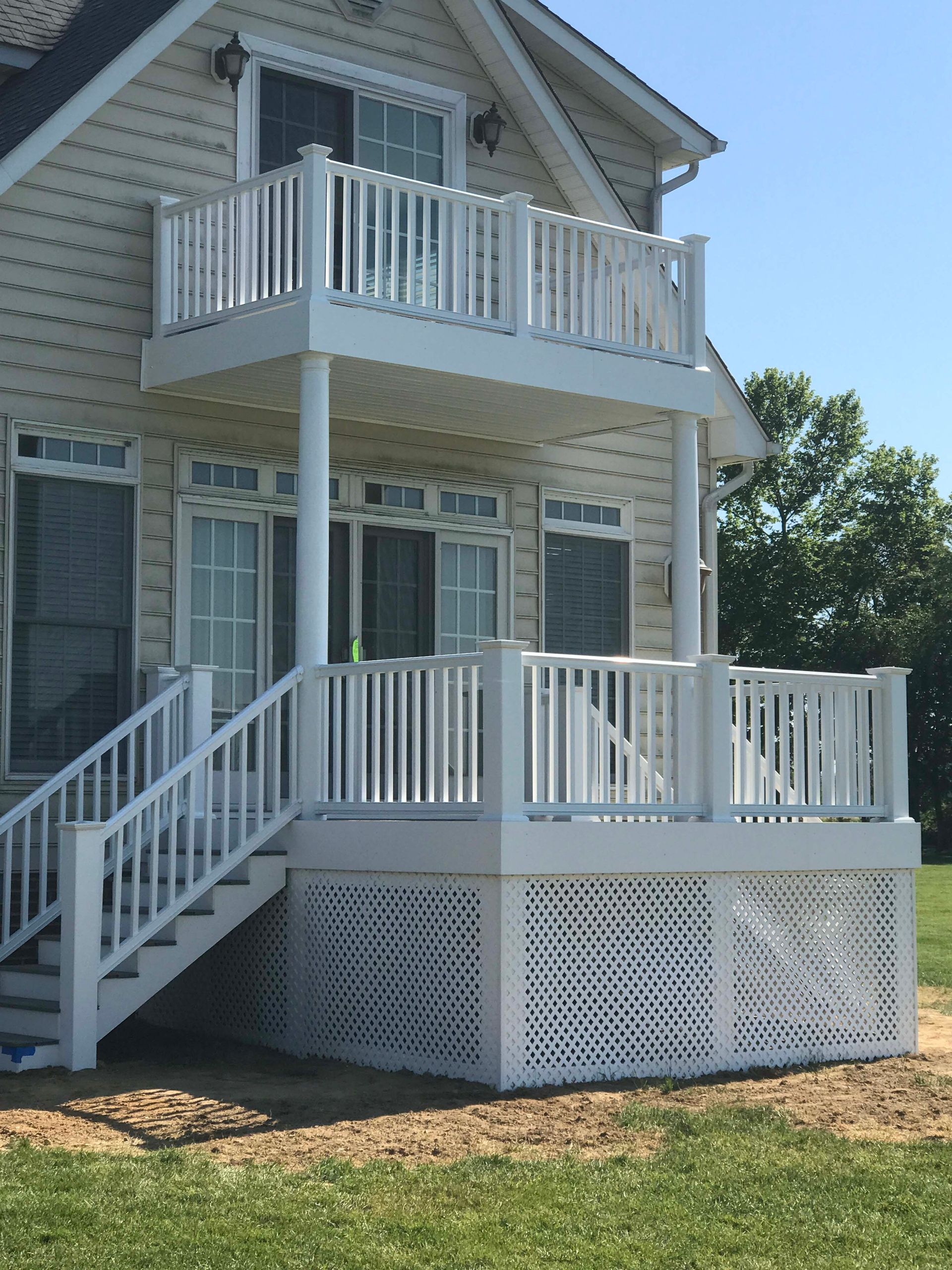 Two-story gray house with white railings and wraparound porch in sunlight