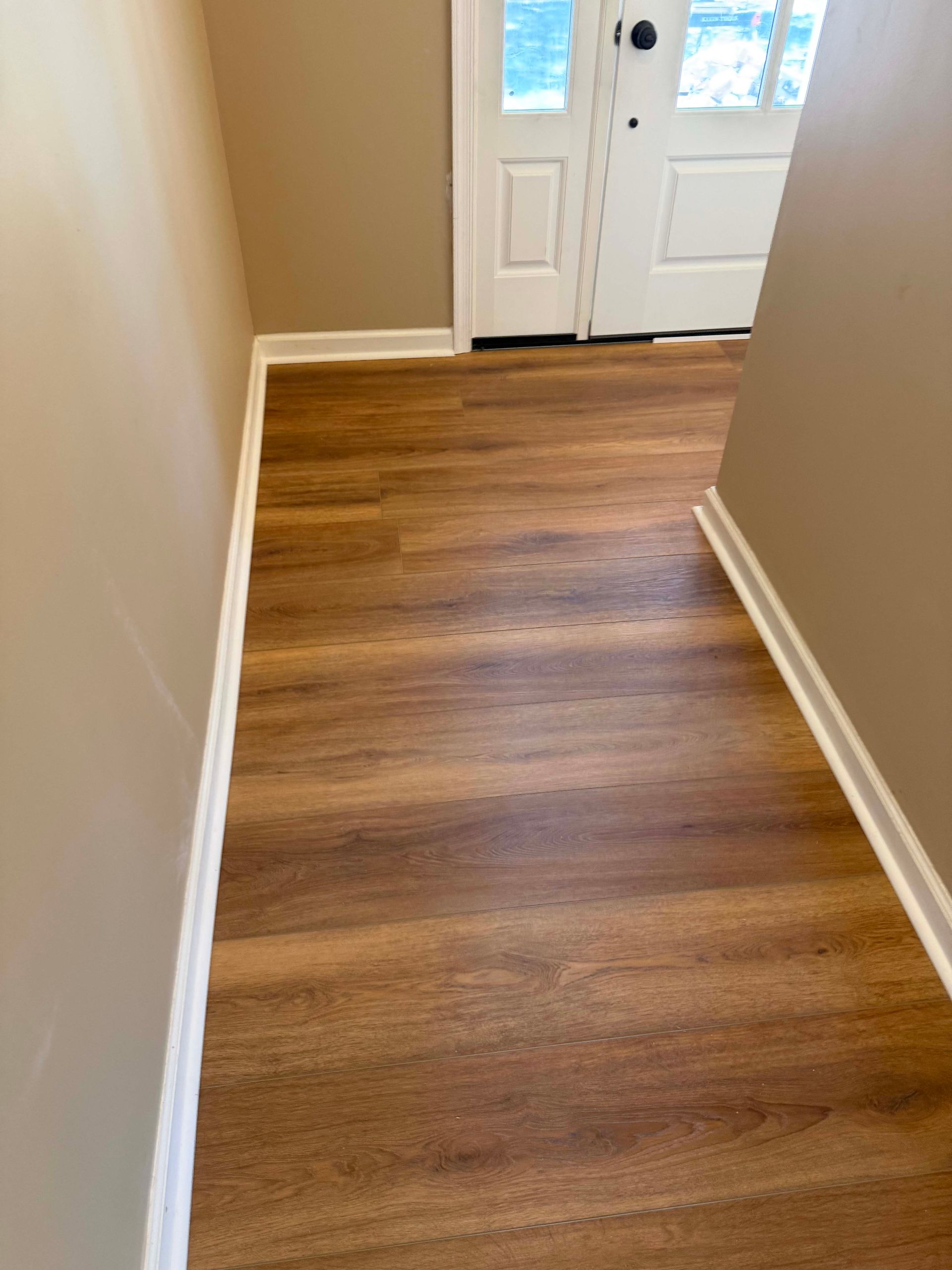 Empty hallway with wood-look flooring and white double doors at the end.