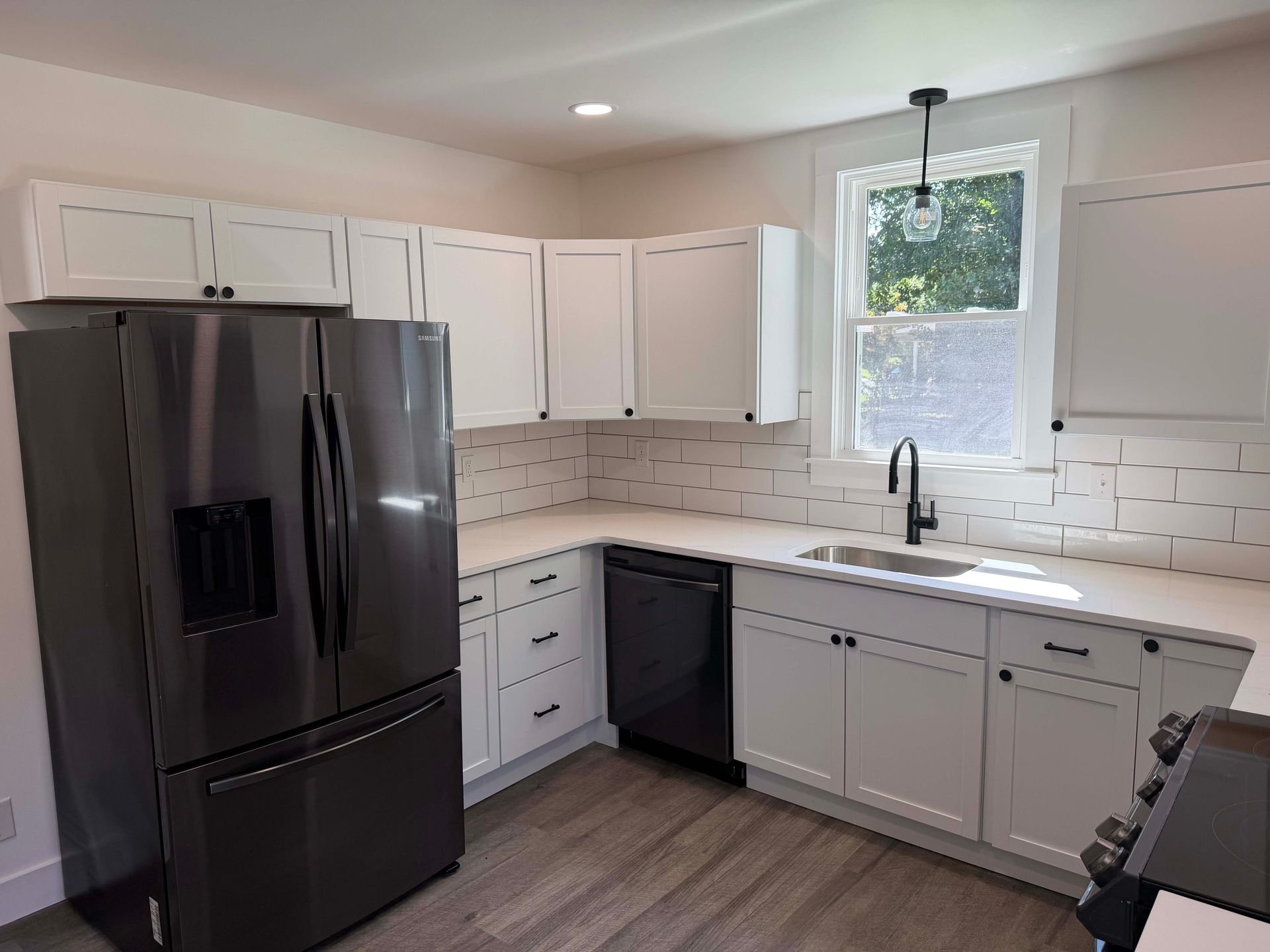 Modern kitchen with white cabinets, black appliances, window over sink, and light wood floor