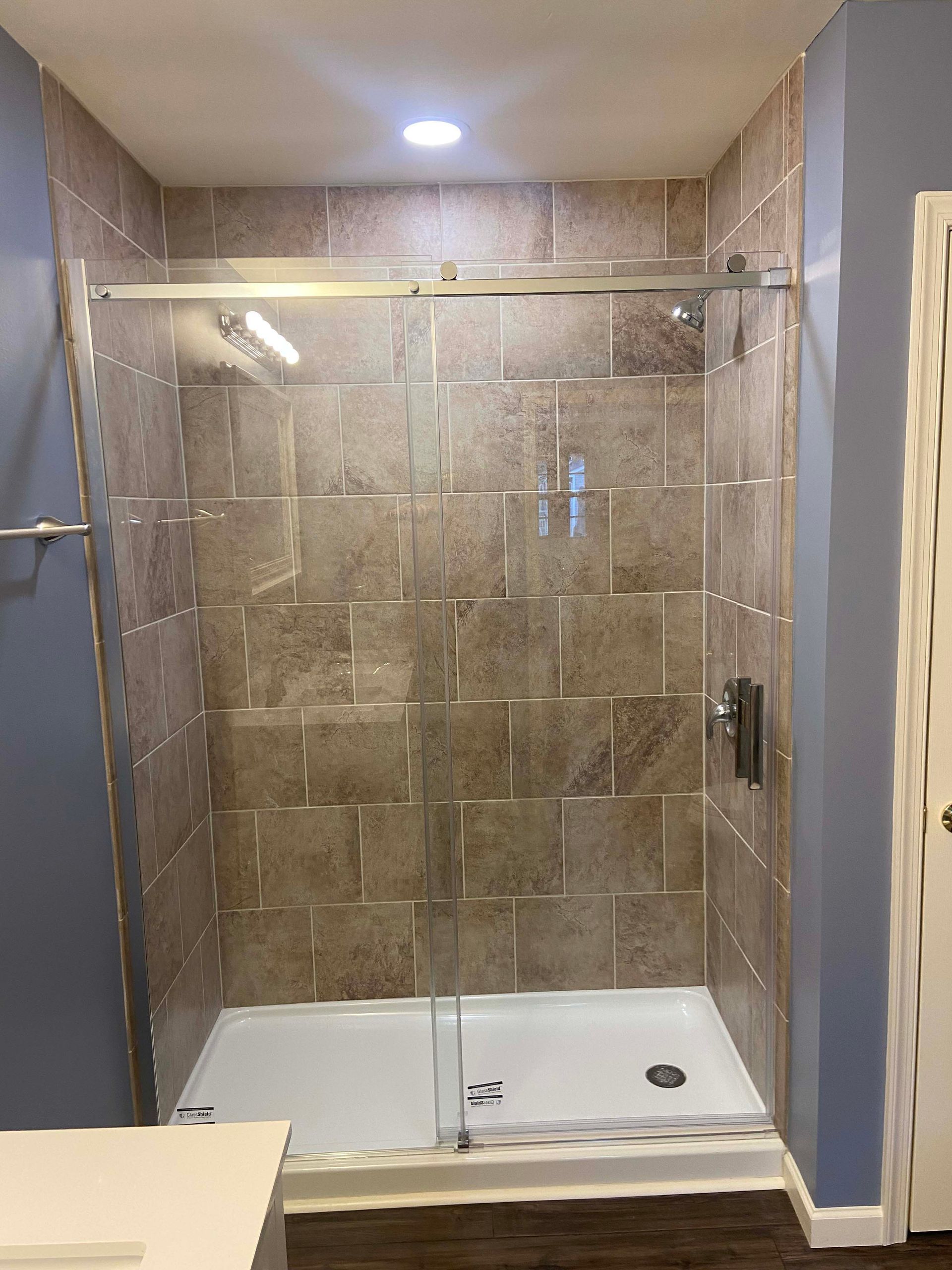 Bathroom with walk-in shower, glass door, beige tile walls, and a built-in bench.