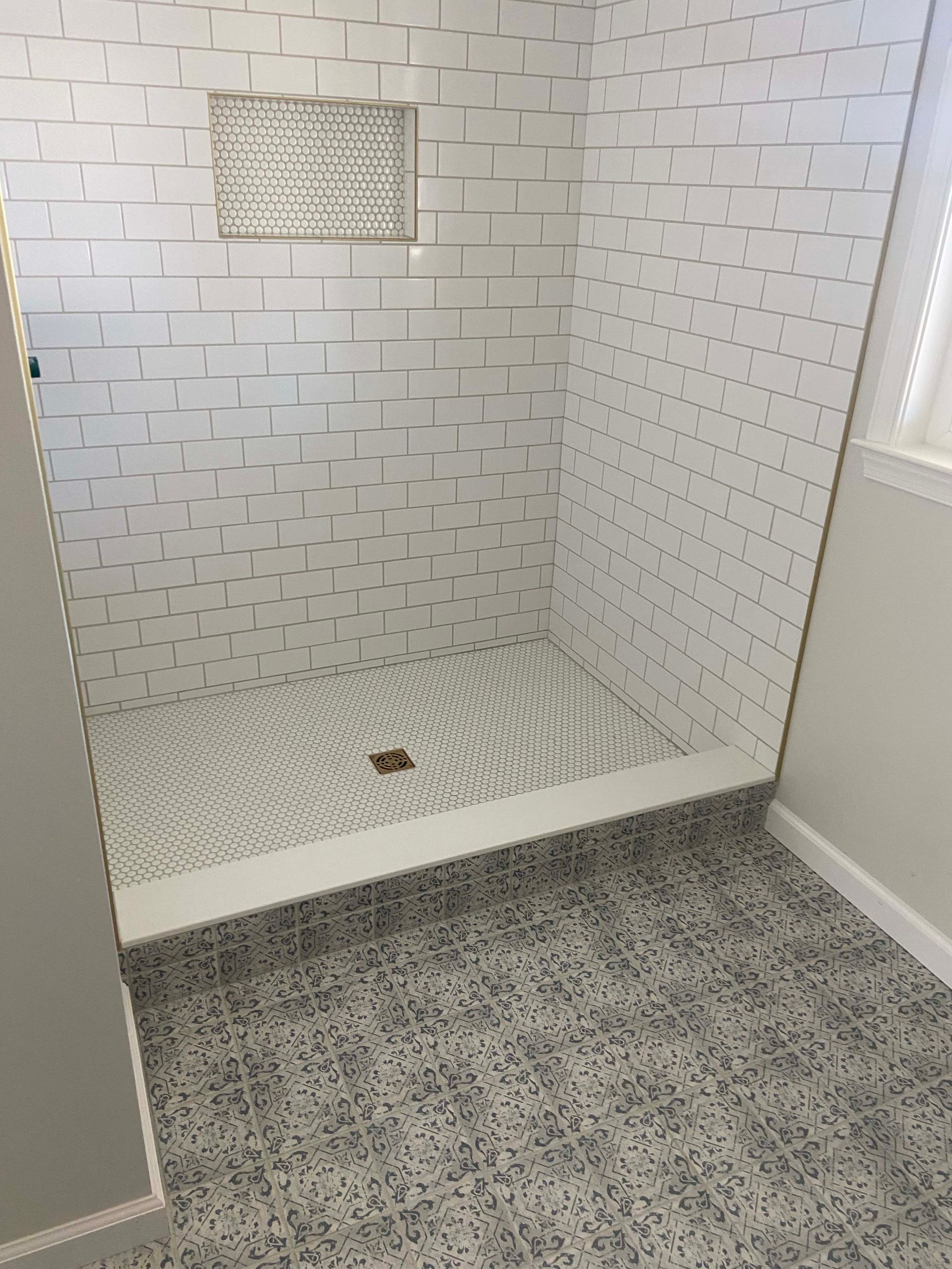 Tiled walk-in shower with mosaic floor and bench, seen from the bathroom doorway.