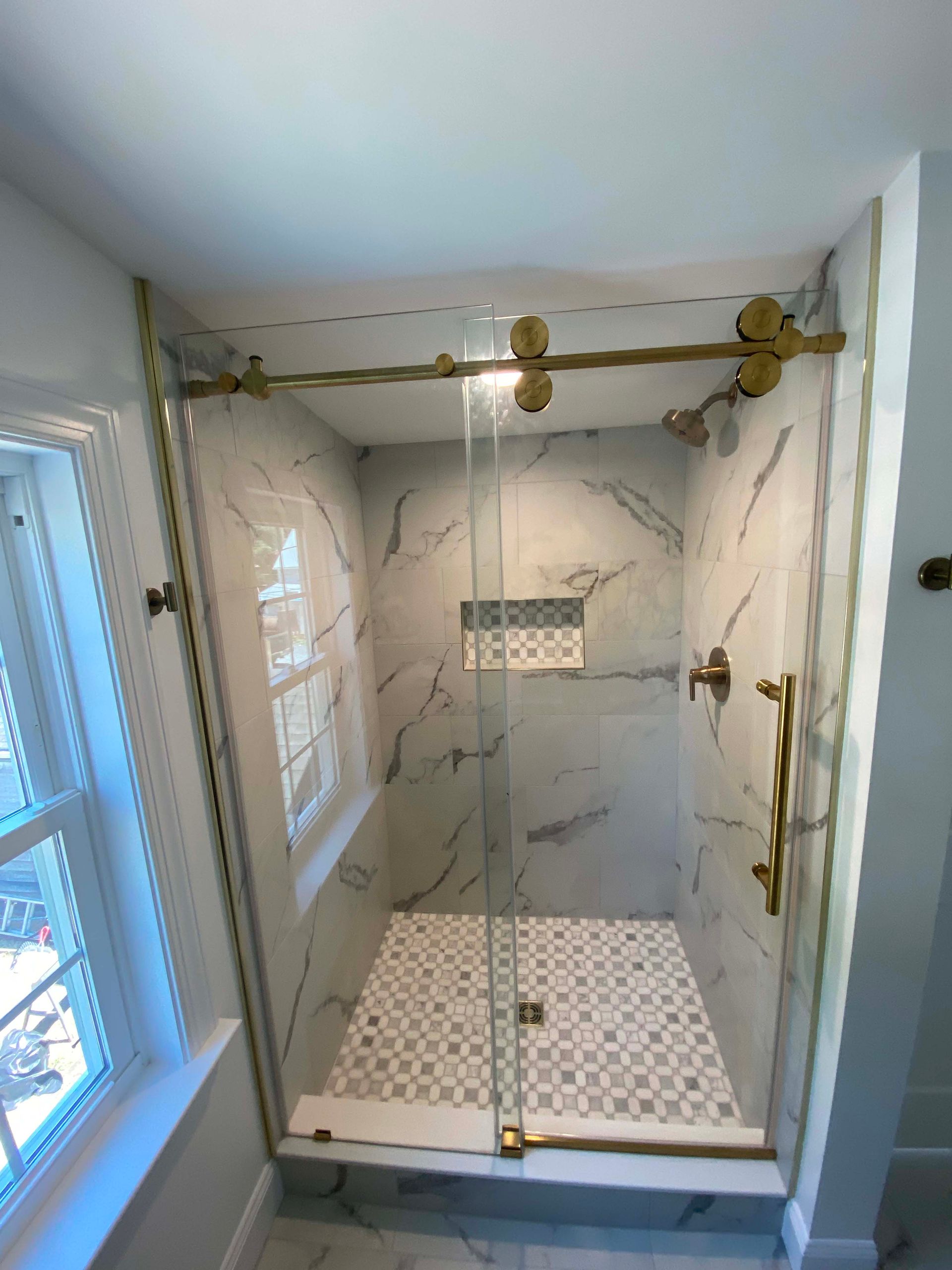 Luxurious glass shower with marble tile, brass fixtures, and hexagon floor in a bright bathroom