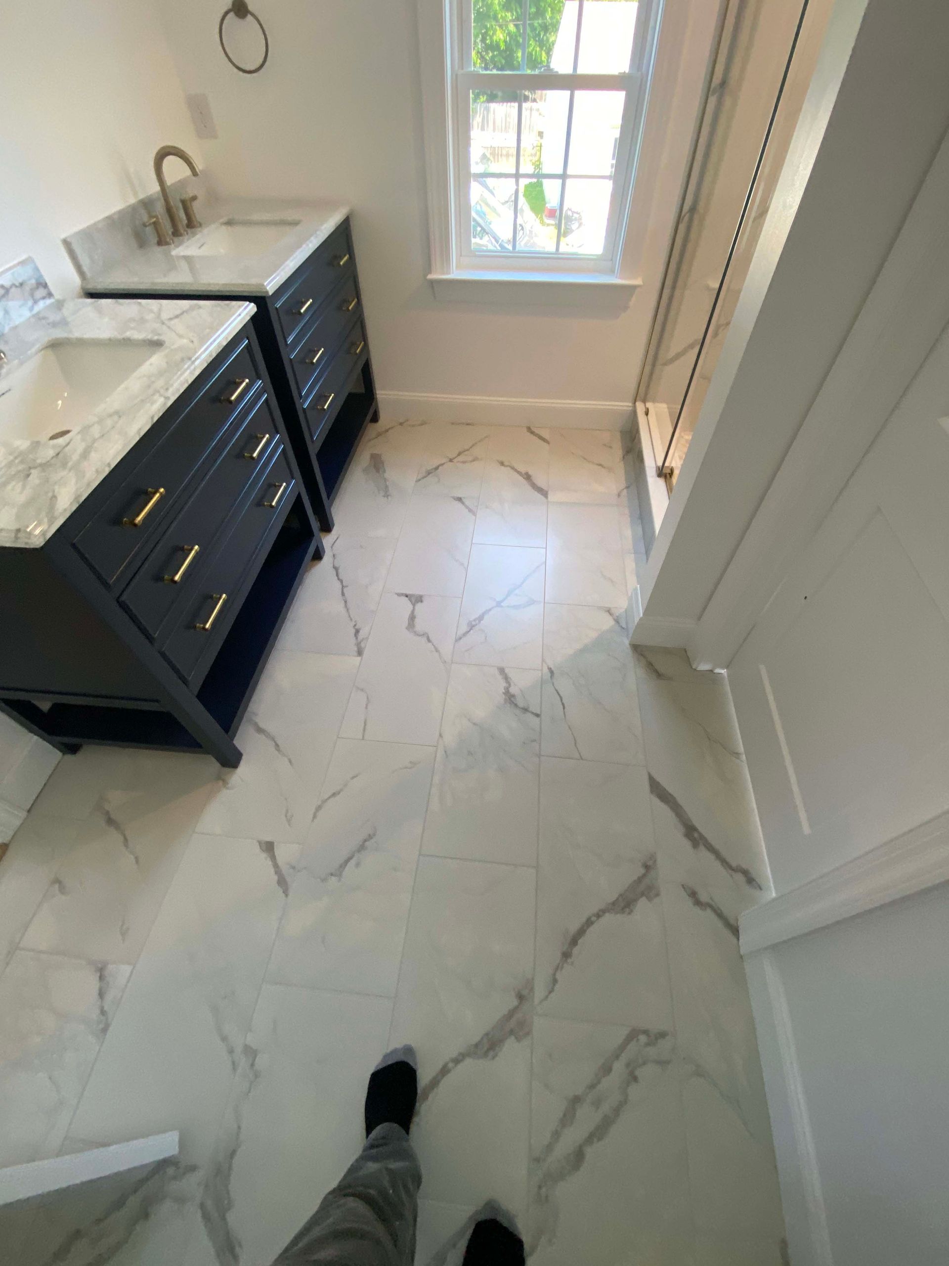 Bathroom with black vanity, white marble-pattern floor, and window light.