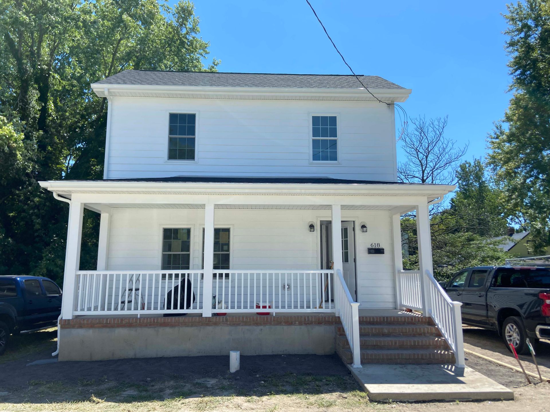 White two-story house with a front porch, steps, and a parked truck beside it under a blue sky
