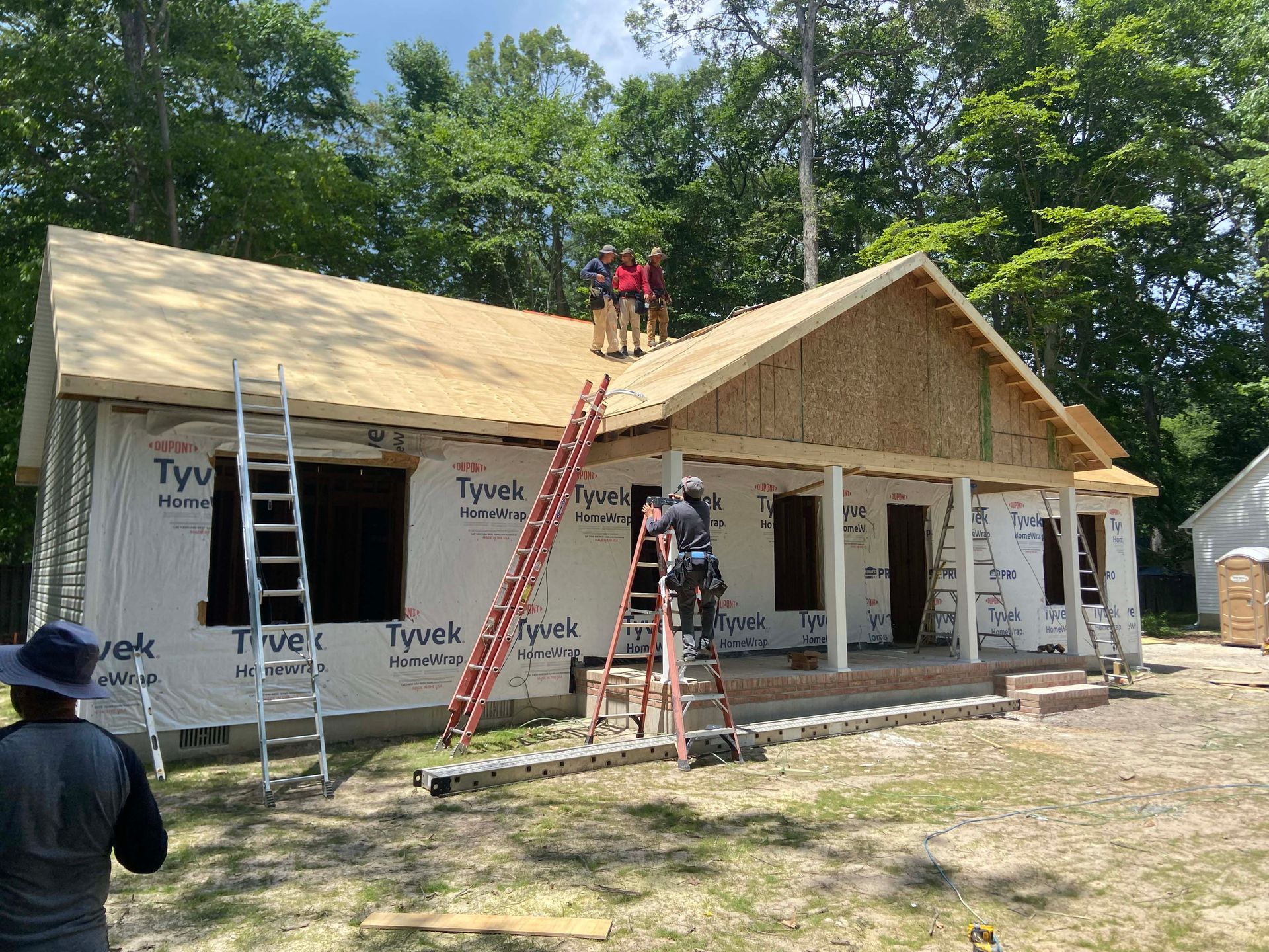 Workers installing a roof on a new house under construction, with ladders and exposed framing.